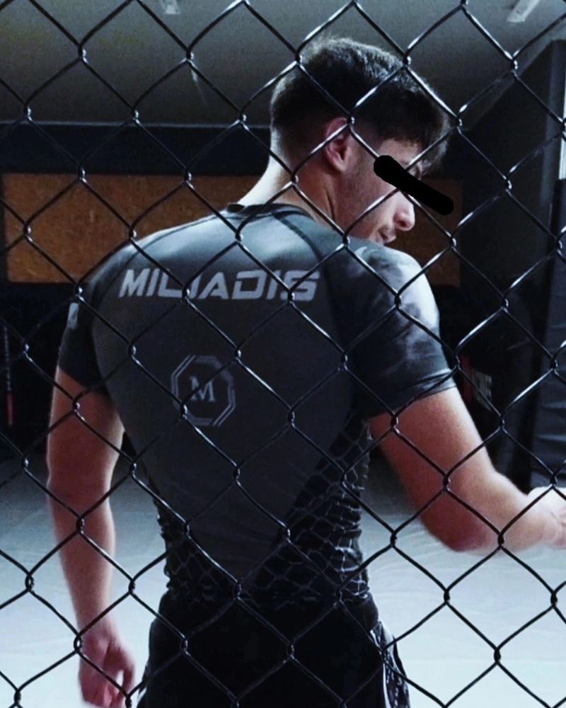 Miliadis Nikos (Μηλιάδης Νίκος), Greek MMA fighter, in a fight shirt seen through the cage fence